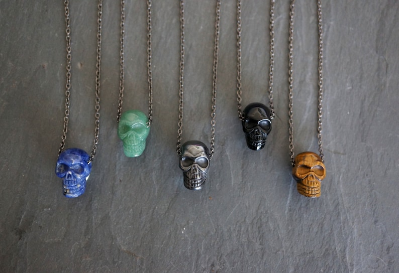 May include: Five silver chains with skull pendants made of different colored stones. The stones are blue, green, black, and brown.