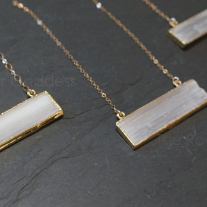 Pode incluir: Quatro colares de ouro com pingentes retangulares de cristal de selenite. Os colares s&atilde;o exibidos em uma superf&iacute;cie preta.