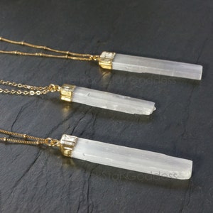 Op de afbeelding: Drie seleniet kristallen kettingen met goudkleurige metalen accenten. De kettingen hebben een gouden ketting met kleine kralen en een rechthoekige seleniet kristallen hanger. De hangers zijn wit en hebben een natuurlijke, getextureerde uitstraling.