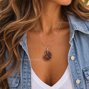 May include: A silver chain necklace featuring a dark brown, spiral-shaped ammonite fossil pendant. The pendant displays a natural, segmented shell pattern with deep reddish-brown tones and a polished finish, suspended from a delicate silver link chain.