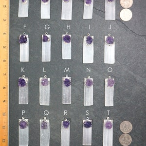 May include: Twenty selenite crystal pendants with amethyst clusters, arranged in rows labeled A through T. Each pendant is approximately 1.5 inches long and features a silver bail. A U.S. quarter is included for scale.