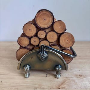 May include: A set of circular wood slice coasters stacked within a semi-circular metal holder. The holder features a brass-toned finish, a central lion head emblem, and two claw-shaped feet. The wood slices show natural grain and bark edges.