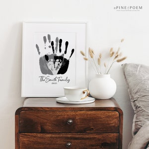 Family handprint art print with baby footprint heart. Customized with family name, colors and year. Design is displayed in a white frame in a modern farmhouse setting.
