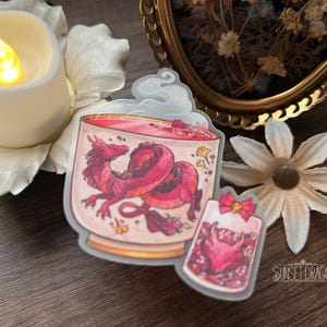 May include: Two stickers featuring a red dragon design. One sticker shows a dragon inside a glass, the other shows a dragon inside a small container with a bow. The stickers are on a wooden surface with a candle and a flower.