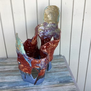 Può includere: Una scultura in ceramica con un design astratto. La scultura è realizzata in argilla rossa, blu e verde e ha una superficie testurizzata.