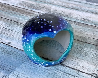 May include: A ceramic heart-shaped hideaway for small animals, painted in shades of blue, green, and purple with white polka dots.