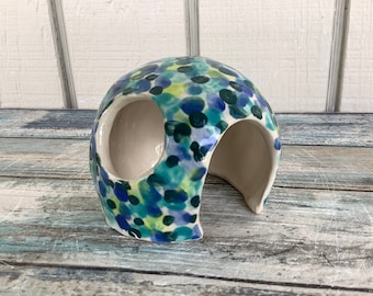 May include: A ceramic hideaway for small pets, painted with a blue, green and white polka dot pattern. The hideaway has two openings for easy access.