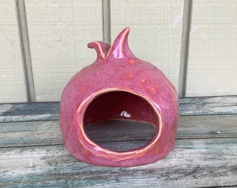 May include: A pink ceramic pomegranate shaped hideaway for small animals. The hideaway has a large opening on one side.