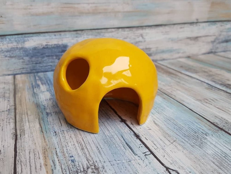 May include: A bright yellow ceramic hide for small animals, featuring a large opening and a smaller hole on the side.