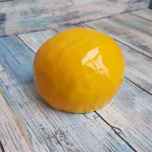 May include: A bright yellow ceramic skull with a glossy finish. The skull is sitting on a light blue and white wooden surface.