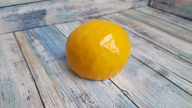 May include: A bright yellow ceramic skull with a glossy finish. The skull is sitting on a light blue and white wooden surface.
