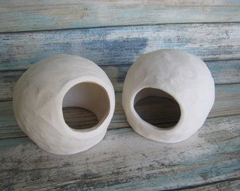 May include: Two white ceramic spherical planters with a hole in the side. The planters are sitting on a light blue and white wooden surface.