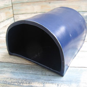 May include: A dark blue ceramic half-cylinder shaped planter with a smooth, glossy finish. The planter is open on one side, creating a curved opening.