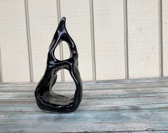 May include: A black ceramic sculpture with an abstract, organic shape. The sculpture has a smooth, glossy finish and features several openings.