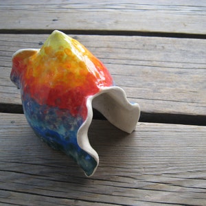 May include: A colorful ceramic planter with a unique, abstract design. The planter is painted in shades of red, orange, yellow, blue, and white.