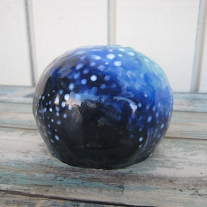 May include: A blue and white ceramic skull with a speckled pattern. The skull is painted with white dots on a dark blue background, with a lighter blue gradient at the top.
