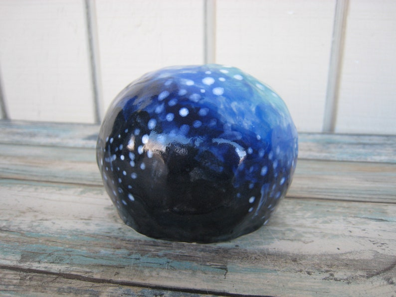 May include: A blue and white ceramic skull with a speckled pattern. The skull is painted with white dots on a dark blue background, with a lighter blue gradient at the top.