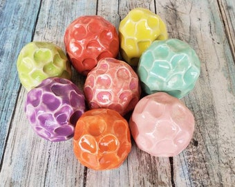 May include: Eight colorful ceramic balls with a textured surface. The balls are in shades of green, yellow, orange, pink, and purple.