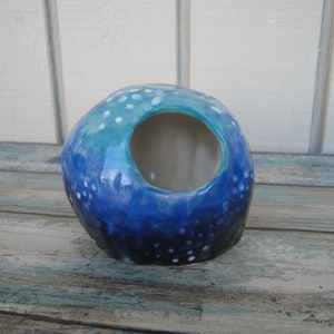 May include: A blue and white ceramic planter with a speckled glaze and a round opening. The planter is shaped like a sphere and has a mottled blue and white glaze.