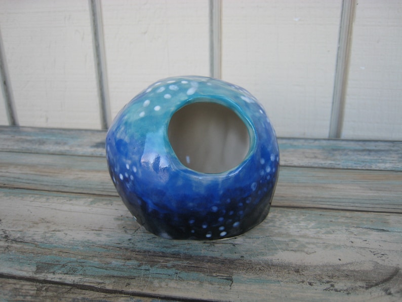 May include: A blue and white ceramic planter with a speckled glaze and a round opening. The planter is shaped like a sphere and has a mottled blue and white glaze.