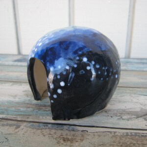 May include: A blue and white ceramic cave with a small opening. The cave is glazed with a dark blue and white speckled design.
