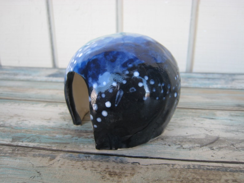 May include: A blue and white ceramic cave with a small opening. The cave is glazed with a dark blue and white speckled design.