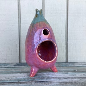 Könnte beinhalten: Eine Keramikskulptur mit rosa und blauem Überzug. Sie hat eine große Öffnung vorne und vier Beine.