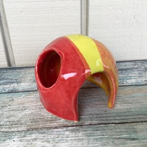 May include: A red and yellow ceramic hide for small animals, with a rounded opening and a smooth, glazed finish.