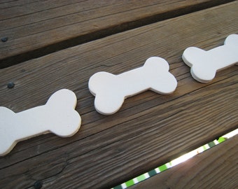 May include: Three white ceramic dog bone shaped ornaments on a wooden surface.