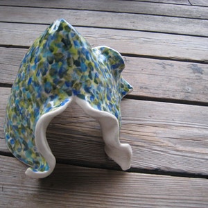 May include: A ceramic sculpture in the shape of a cave with a white interior and an exterior covered in a blue, green, and yellow abstract pattern.