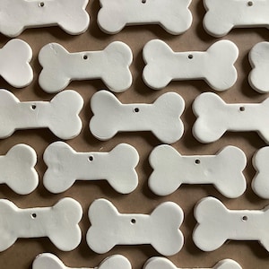 May include: A collection of 20 white ceramic bone-shaped ornaments. The ornaments are all the same size and shape, and they have a hole at the top for hanging.