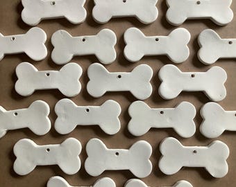 May include: A collection of 20 white ceramic bone-shaped ornaments. The ornaments are all the same size and shape, and they have a hole at the top for hanging.