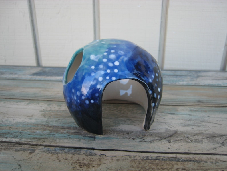 May include: A blue and white ceramic hide for small animals, with a round shape and a large opening. The hide is decorated with white dots and a blue and green gradient.