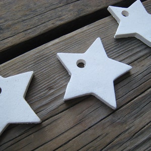 Puede incluir: Tres estrellas de cerámica blanca con un agujero en el centro. Las estrellas están dispuestas en fila sobre una superficie de madera.