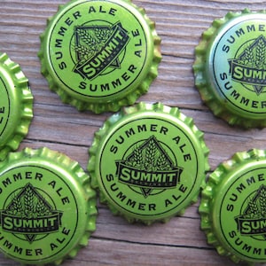 May include: Six green bottle caps with the words "Summit Brewing Co." and "Summer Ale" printed on them. The bottle caps are arranged in a circle on a wooden surface.