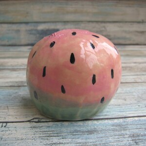 May include: A ceramic watermelon shaped ornament with a pink and green glaze and black painted seeds.