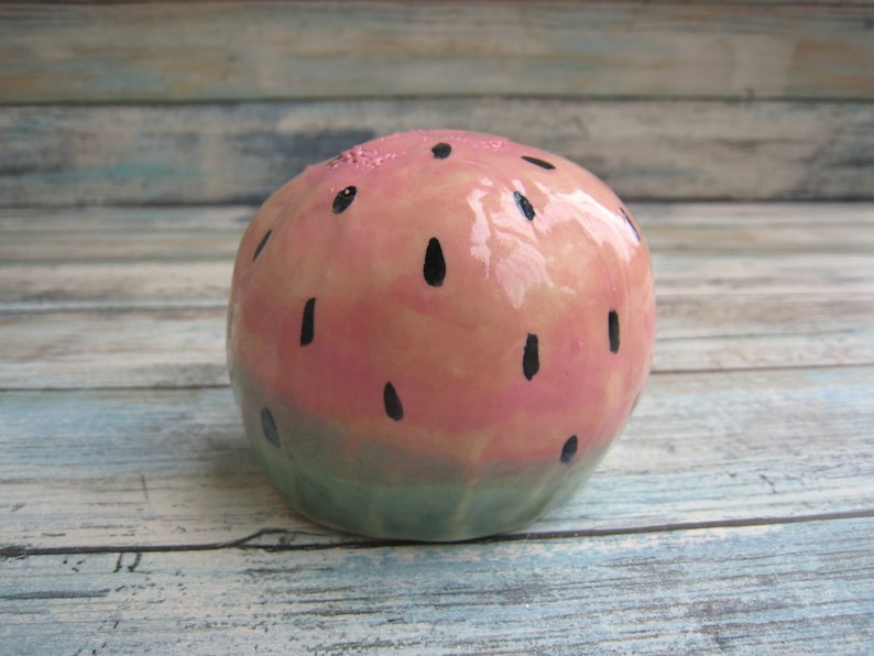 May include: A ceramic watermelon shaped ornament with a pink and green glaze and black painted seeds.