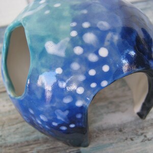 May include: A blue and white ceramic planter with a speckled glaze and a large opening on the side. The planter is shaped like a dome and has a smooth, glossy finish.