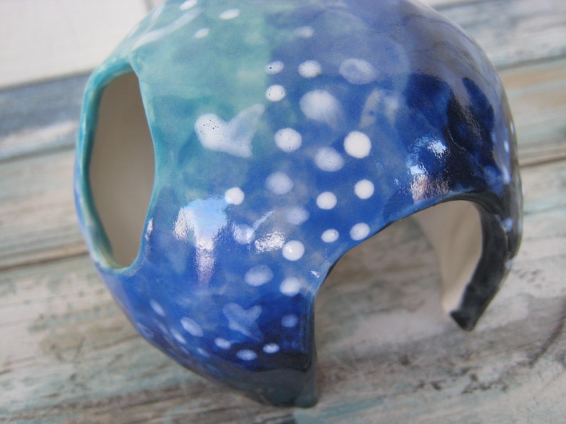 May include: A blue and white ceramic planter with a speckled glaze and a large opening on the side. The planter is shaped like a dome and has a smooth, glossy finish.