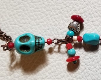 Southwest inspired turquoise color skull bead with dangling charms of Turquoise and Coral beads and silver heart.