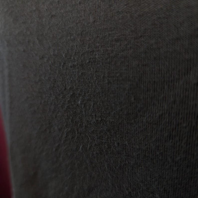May include: Close-up of a dark grey fabric with a textured surface. The fabric appears to be a knit or woven material, with small fibres visible on the surface. The image highlights the texture and colour of the textile.