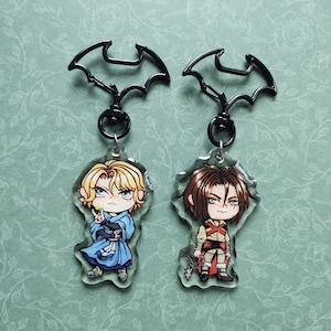 May include: Two clear acrylic keychains with black bat-shaped clips. Each keychain features a cartoon character with a different hairstyle and outfit. One character has blonde hair and is wearing a blue and white outfit. The other character has brown hair and is wearing a red and brown outfit.