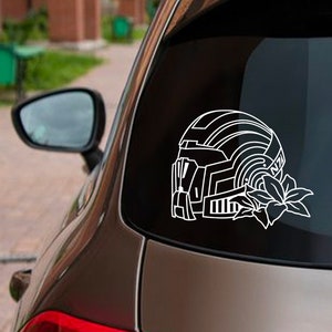 May include: A white vinyl decal of a futuristic helmet with a flower design. The decal is on the back window of a car.