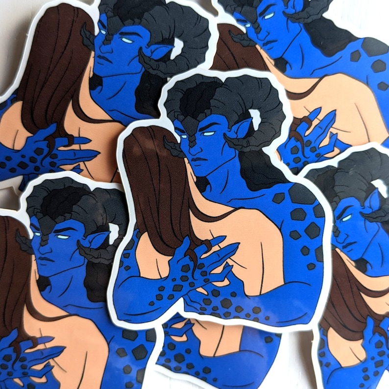 May include: A set of stickers featuring a blue-skinned, horned creature with black horns and a black and blue patterned body. The creature is embracing a person with long brown hair. The stickers are printed on white paper.