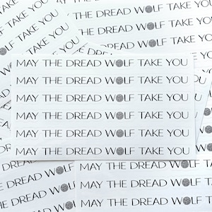 May include: A sheet of white stickers with the phrase "May the Dread Wolf Take You" repeated multiple times. The phrase is written in a black, stylized font with a wolf's head symbol.