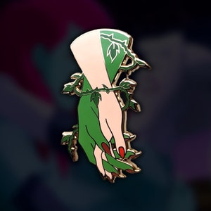 Puede incluir: Pin de esmalte dorado con una mano estilizada, mitad verde y mitad color piel. La mitad verde está cubierta de enredaderas y hojas.