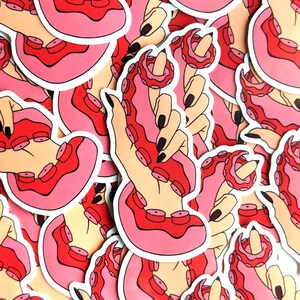 May include: A set of stickers featuring a hand holding an octopus with pink and red tentacles. The stickers are printed on white paper and have a glossy finish.