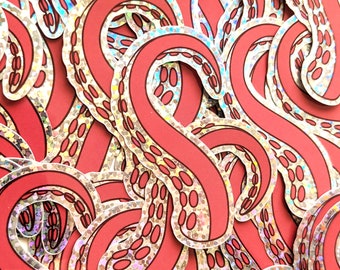May include: A close-up of a pile of red and silver holographic stickers featuring an octopus tentacle design.