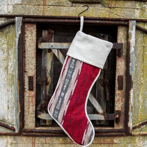 May include: A red and white patterned Christmas stocking with a white cuff hangs from a hook on a rusty metal door.
