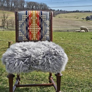 May include: A wooden chair with a gray faux fur seat cushion and a patterned fabric back. The chair is in a field with a green grassy background.